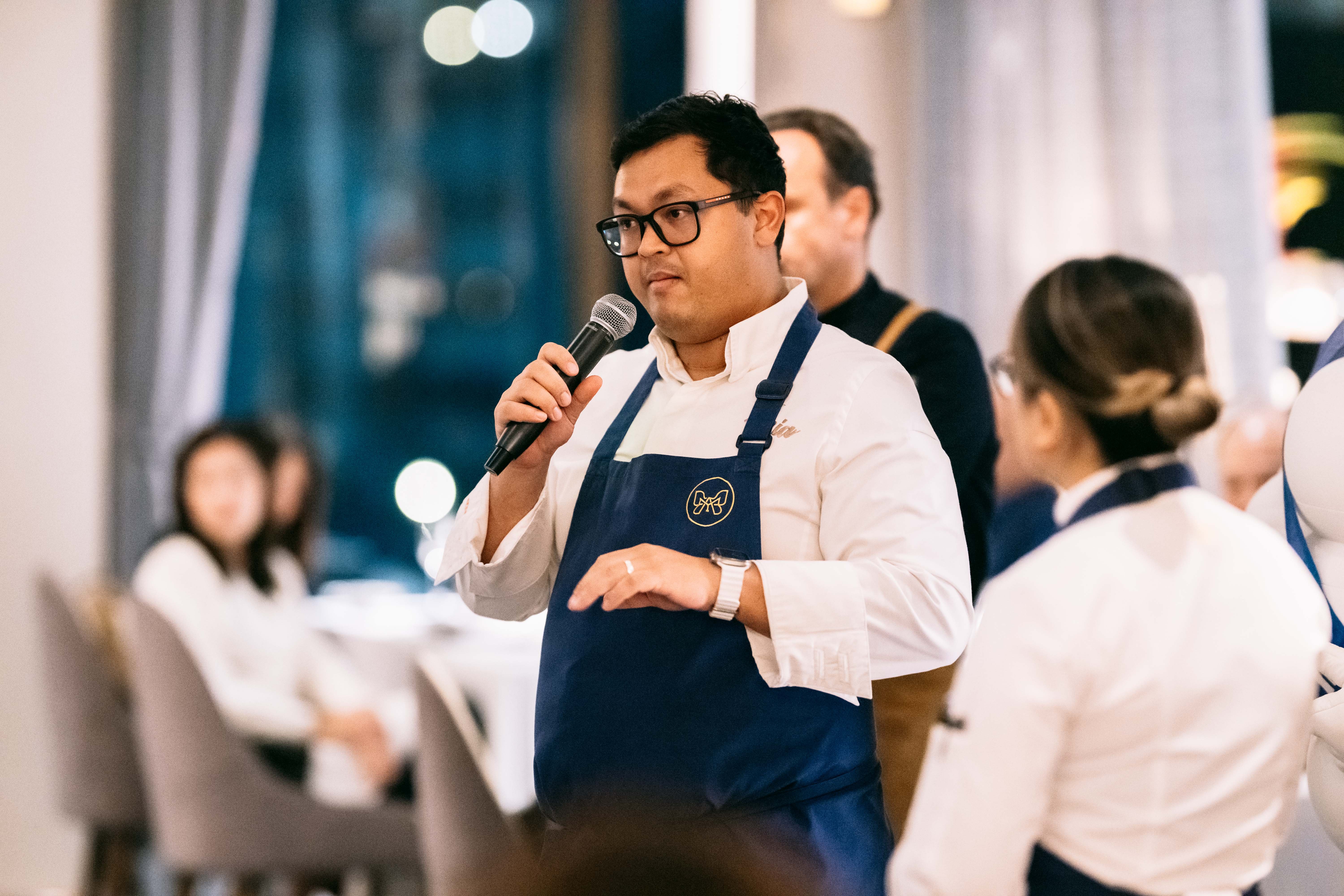 Chef Top Russell speaking at an off-site event, wearing the Mia apron